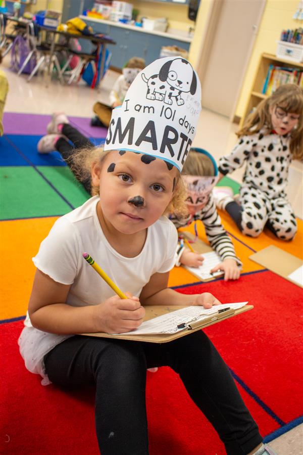 girl dressed as dalmatian dog writing on clipboard